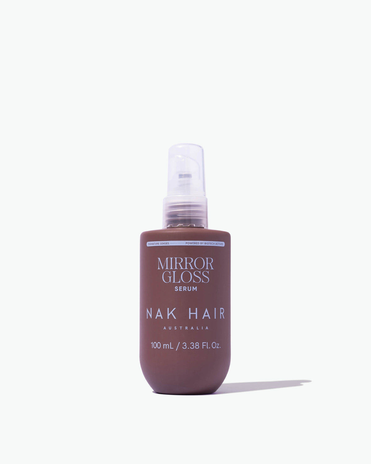 A bottle of NAK HAIR Australia Mirror Gloss Serum, 100 mL, featuring a dark brown bottle and a clear spray nozzle, set against a plain white background with a soft shadow.
