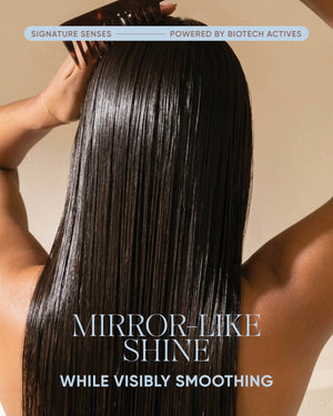 A person shown from the back with long, straight, glossy dark hair and arms raised, holding a comb near the scalp. Text at the top reads 'SIGNATURE SENSES POWERED BY BIOTECH ACTIVES' and the lower text reads 'MIRROR-LIKE SHINE WHILE VISIBLY SMOOTHING.
