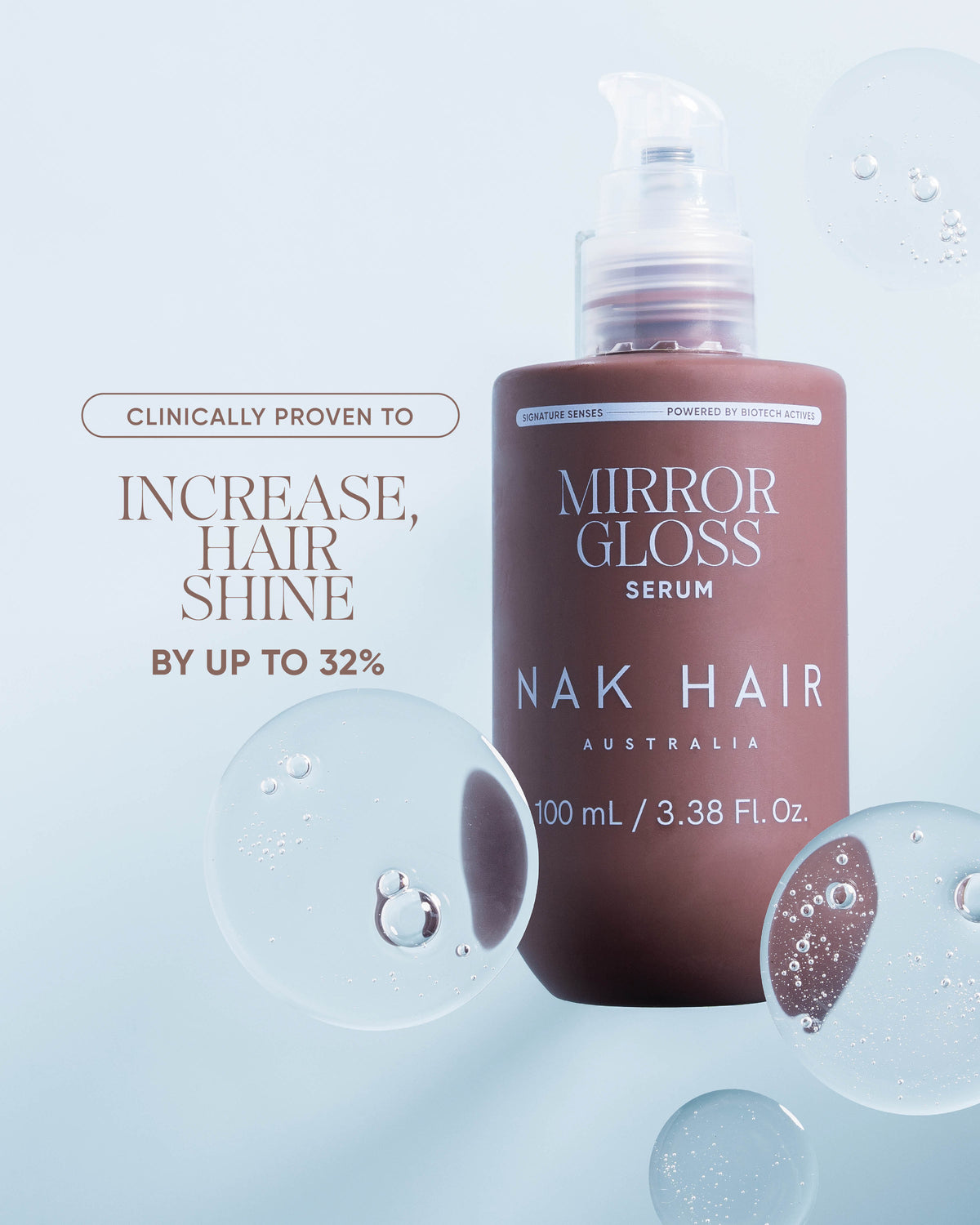 A bottle of Mirror Gloss Serum by NAK Hair Australia, displayed against a light blue background with decorative water droplets. The bottle is a dusty rose-brown color with white text.